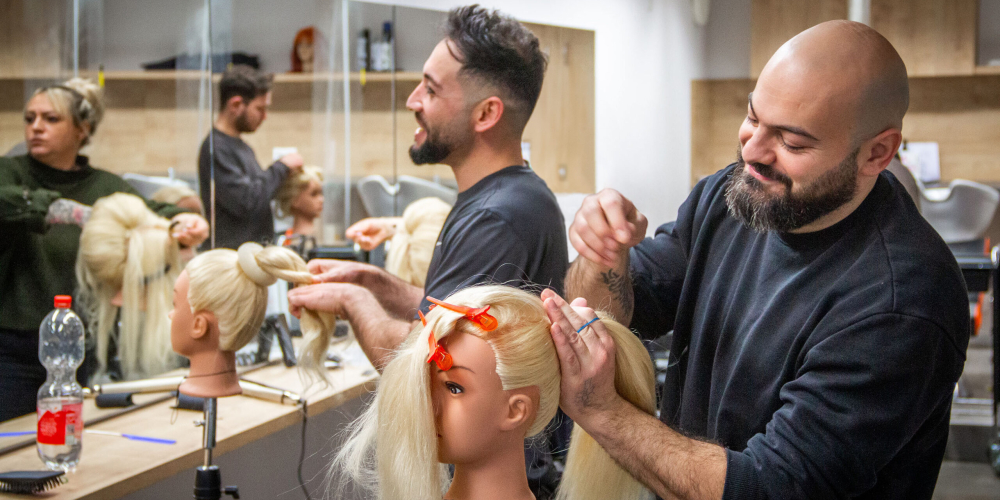 Friseur schneidet und frisiert das Haar einer Übungspuppe mit blonden Haaren und Haarspangen.
