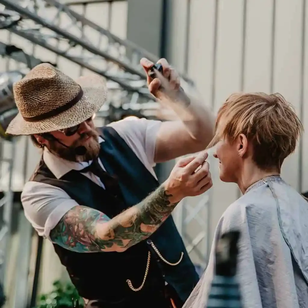 Friseur mit Hut schneidet das Haar eines Kunden während einer Frisurenpräsentation.