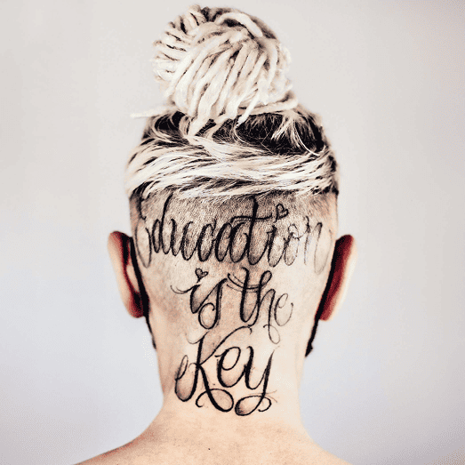 Hinteransicht eines Kopfes mit einem Haarschnitt und einer Tätowierung, die den Text 'education is the key' zeigt.