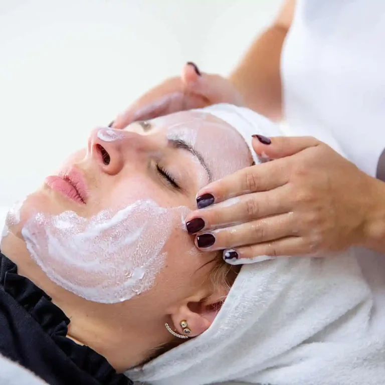 Frau mit geschlossenen Augen erhält eine Gesichtsbehandlung mit einer weißen Maske auf ihrem Gesicht.