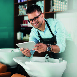 Friseur, der ein Tablet in einem Salon benutzt, während er an einem Waschbecken steht.