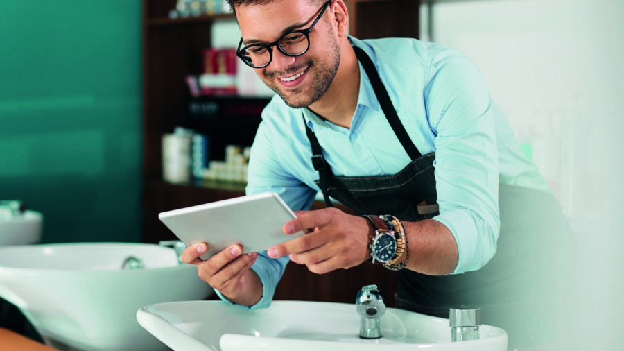 Friseur, der ein Tablet in einem Salon benutzt, während er an einem Waschbecken steht.
