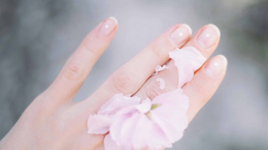 Eine Hand mit rosa Blütenblättern, die sanft um den Finger gelegt sind.