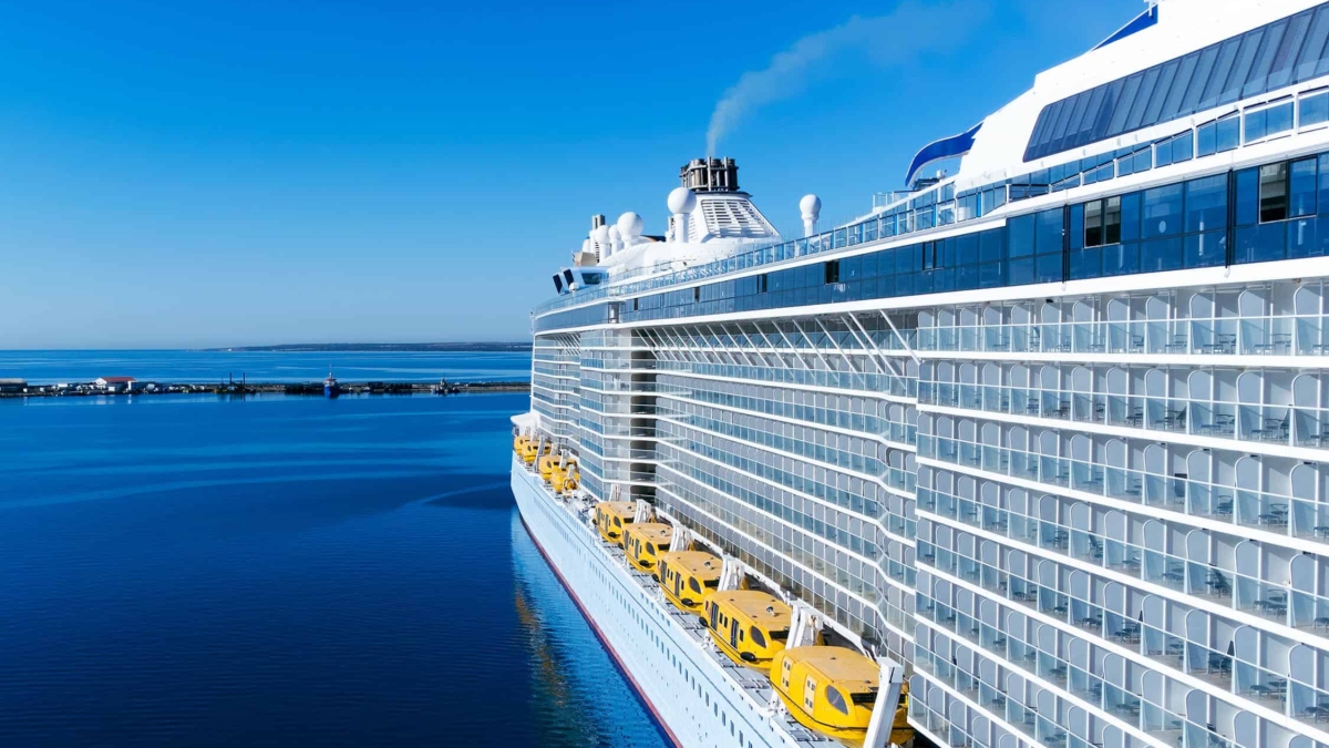Ein großes Kreuzfahrtschiff mit gelben Rettungsbooten an der Seite im Hafen unter blauem Himmel.