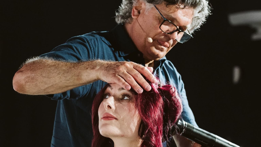 Friseur mit grauen Haaren, der eine Frau mit roten Haaren frisiert und einen Haartrockner verwendet.