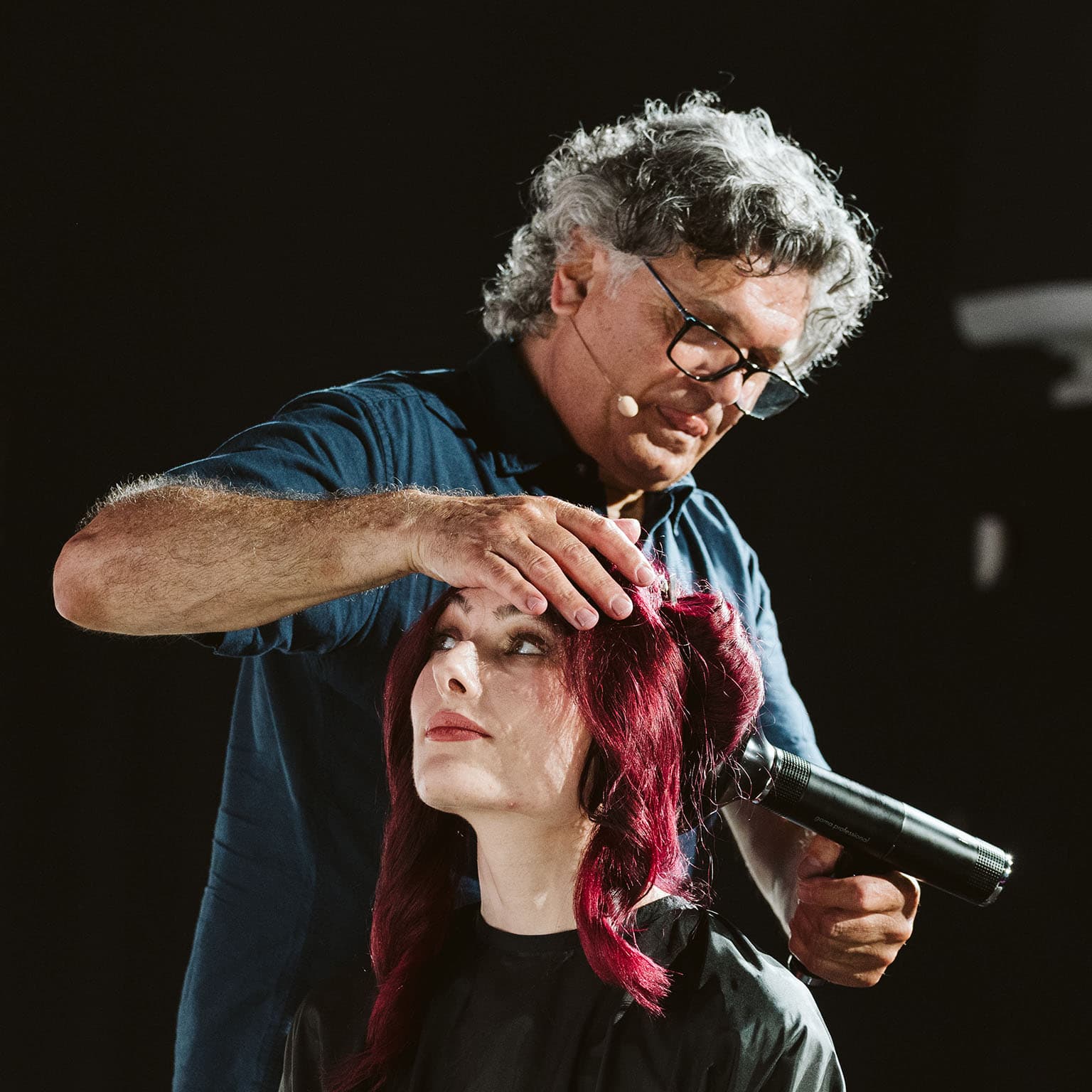 Friseur mit grauen Haaren, der eine Frau mit roten Haaren frisiert und einen Haartrockner verwendet.