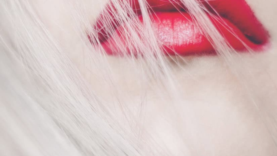 Nahaufnahme von roten Lippen mit blonden Haarsträhnen im Hintergrund.