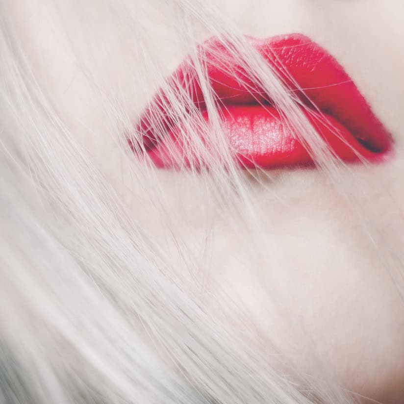 Nahaufnahme von roten Lippen mit blonden Haarsträhnen im Hintergrund.