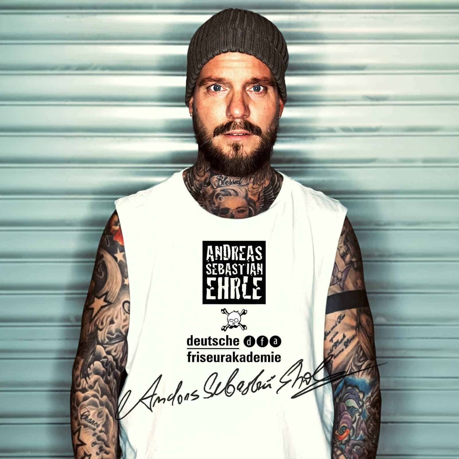 Mann mit Bart und Tattoos trägt ein weißes T-Shirt mit Aufdruck und Mütze.