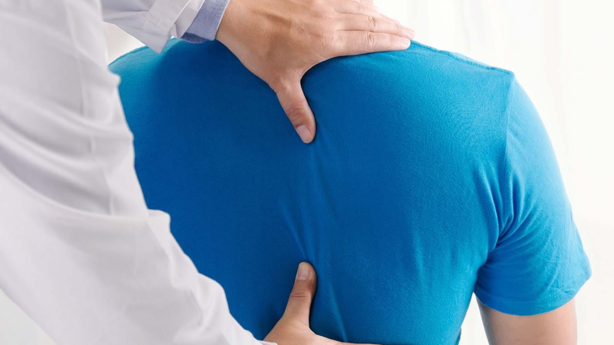 Ein Arzt untersucht einen Patienten im blauen T-Shirt mit einer Hand auf dem Rücken.