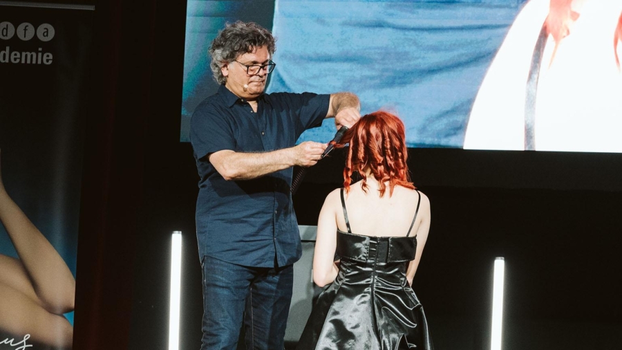 Friseur schneidet das Haar eines Modells mit roten Haaren während einer Vorführung auf einer Bühne.