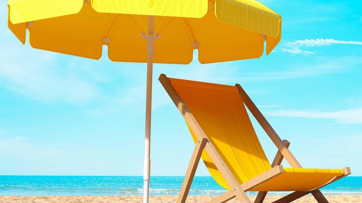 Gelbe Liege und Sonnenschirm auf einem Sandstrand mit Meer im Hintergrund.