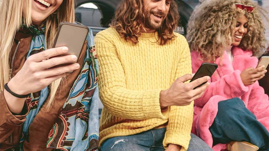 Drei Personen sitzen zusammen und nutzen ihre Smartphones, während sie lächeln und miteinander interagieren.
