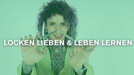 Frau mit lockigen Haaren hält eine Schere in beiden Händen und lächelt in die Kamera.