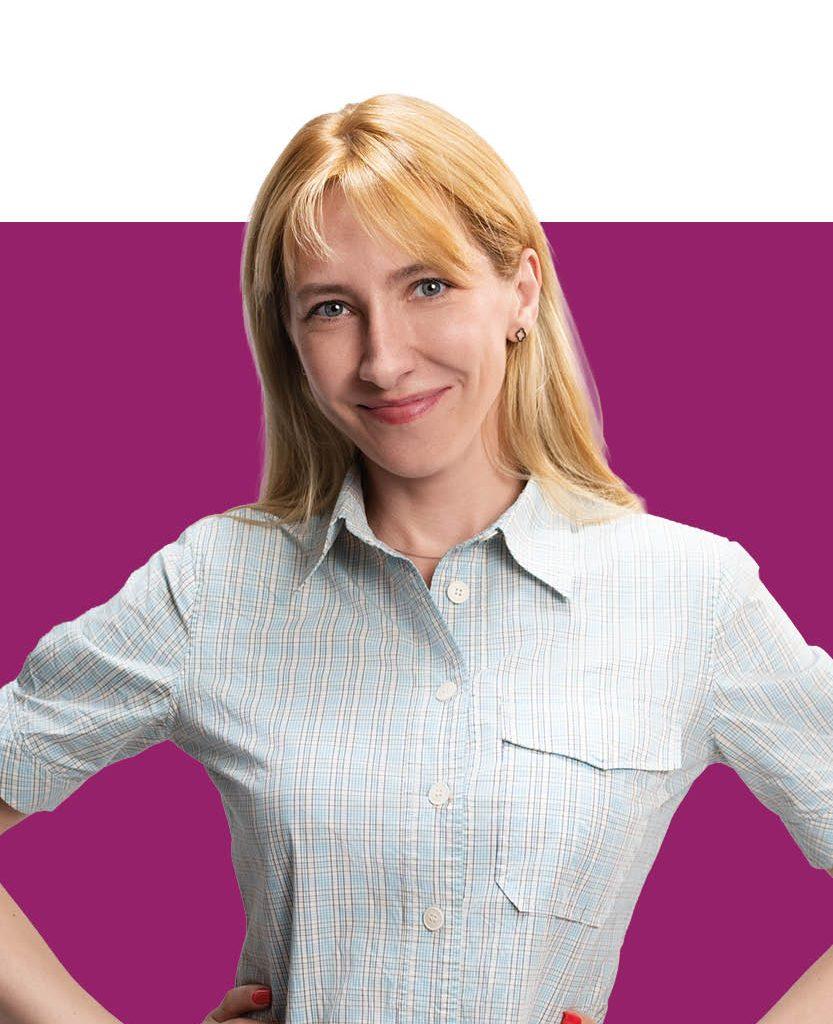 Eine blonde Frau mit blauem Blick und kariertem Hemd steht mit aufgestellten Armen vor weiß-violettem Hintergrund und lächelt ruhig in die Kamera.
